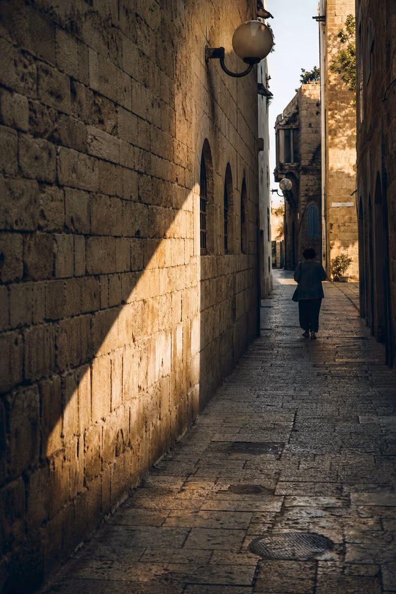 רחוב צר ביפו עם דמות הולכת באור אחר הצהריים